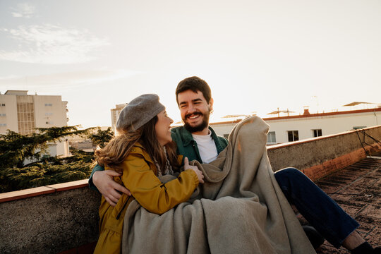 Loving ouple sitting on rootop and hugging during sunset
