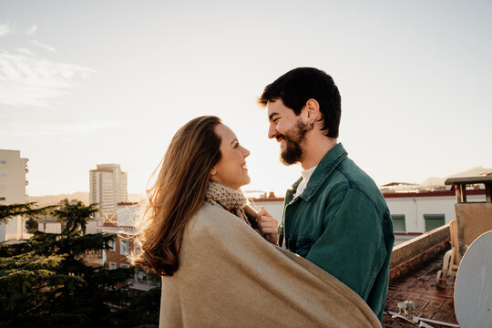 Portrait of cute couple looking at each other and hugging on rooftop during sunset

