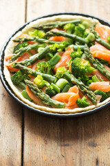 Preparing quiche with salmon, broccoli and green asparagus, coated with milk and eggs mixture. Raw tart - oven ready. 