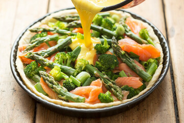 Preparing quiche with salmon, broccoli and green asparagus, coated with milk and eggs mixture. Raw tart - oven ready. 