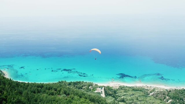 Drone tracking shot of paragliding over the scenic hill and blue sea, extreme sports activities concept.