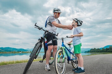 Father and son ride, cycling their bikes together, on sunny day, Happy family in helmets is riding bikes having fun.
