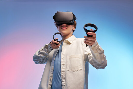 young boy play VR games in virtual reality helmets on bright colourful background, hold controllers and look away. guy in VR helmets play video games. Isolated. VR gaming concept