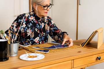 Senior woman repairing a broken plate  and watching tutorials in her tablet