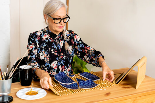 Portrait of hoary woman repairing a broken plate with a millenial japanese technique 