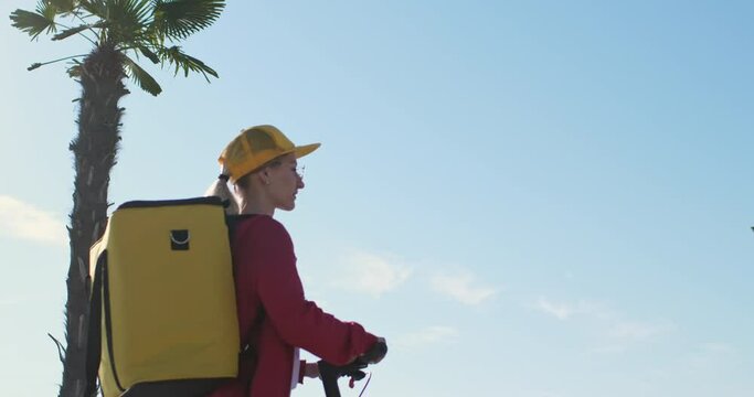 A young girl student delivers parcels and food on an electric scooter with a yellow backpack and a yellow baseball cap, working in a delivery service.