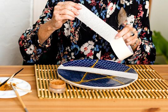Close-up of woman repairing with scotch tape a broken plate 