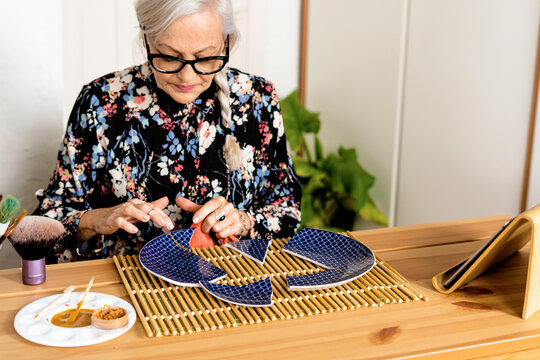 Portrait of hoary woman repairing a broken plate with a millenial japanese technique 