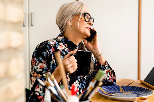 Senior woman talking by phone and doing crafts at home 