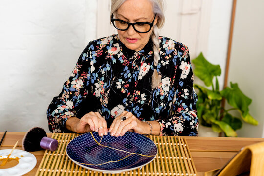 Portrait of hoary woman repairing a broken plate with a millenial japanese technique 