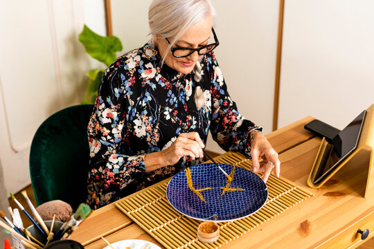 Portrait of hoary woman repairing a broken plate with a millenial japanese technique 