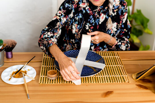 Senior woman putting duct tape to a broken ceramic plate