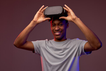 Excited african american man looking at you with smile while taking off vr headset after looking through virtual assortment, experienced virtual reality game, isolated on vinous background
