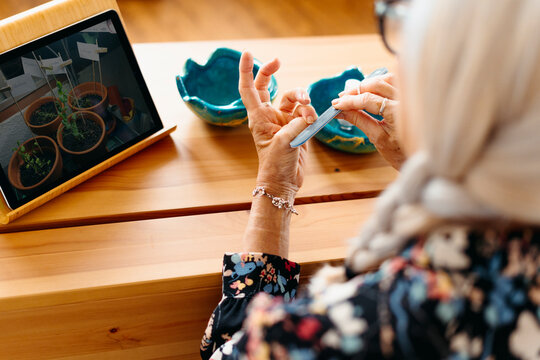 Woman filing her nails and watching videos in her tablet at home