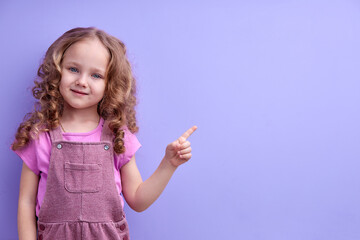 Little girl in pink shirt shows finger at side. Concept for advertising, pay attention to the subject or words. Place for text. Cute, beautiful, smiling child portrait