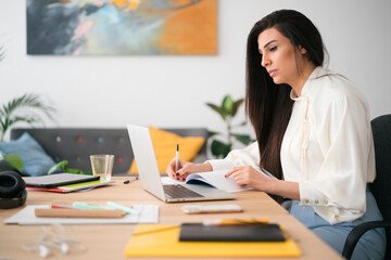 Focused Arab businesswoman working on laptop and taking notes in office