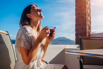 Woman relaxing on hotel terrace drinking morning coffee enjoying Santorini mountain landscape in...
