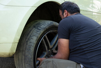 Fototapeta na wymiar The worker serves the car, changing tires on the wheel. Removes or puts on a wheel,