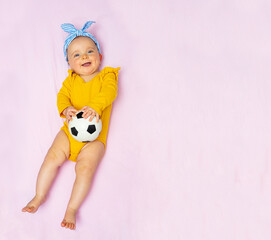 Laughing baby girl lay with football ball in bed