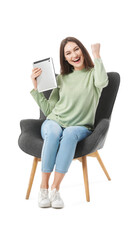 Happy young woman with tablet computer sitting in armchair on white background