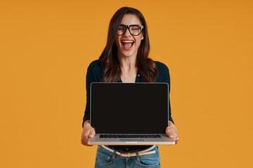 Happy young woman in smart casual clothing pointing copy space at laptop