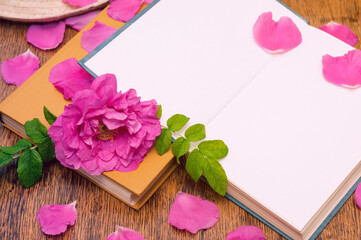 Open book with rosehip flower petals on a wooden table
