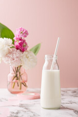 Obraz na płótnie Canvas A bottle of milk on marble table on pink background with pink and white flower bouquet, bright and pastel drink composition vertical