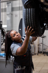 Female car mechanic worker checking, repair and maintenance wheel at auto repair shop. African...