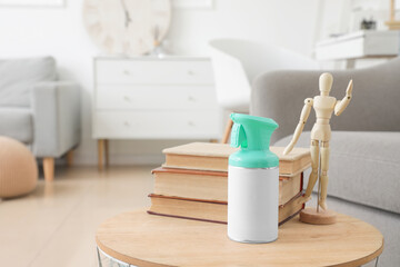 Bottle of air freshener with books and wooden mannequin on table in living room