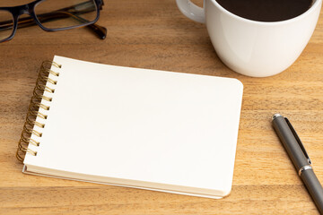 Spiral notepad mockup template with coffee cup and eyeglasses on wooden table. Empty White paper