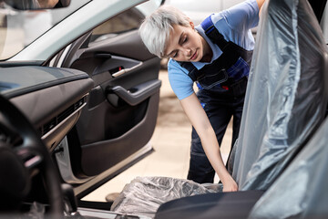female auto mechanic covers polyethylene on car seat so that it does not get dirty. Car repair,...