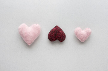 Three knitted hearts on a light gray background.