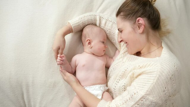 Caring smiling mother lying with her little baby son in diapers and gently stoking him. Concept of parenting ,baby hygiene and child care