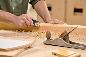 Joiner's works: hands of male carpenter scribbles the board with planer, in workshop, close-up photo of hands of handsome hardworking male engaged in woodworking. copy space