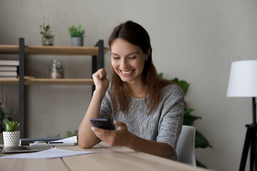 Excited woman reading good news, using smartphone, showing yes gesture, happy young businesswoman...