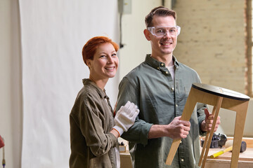 Portrait Of Cheerful Smiling Joiners Making Handmade Chair In Workshop, Cooperating, Looking At...