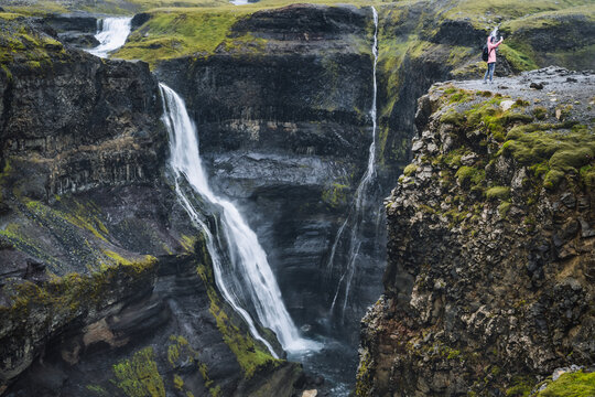 Woman on the edge selfy photographing in front of Granni waterfall and deep narrow gorge. Thjorsardalur valley in Iceland