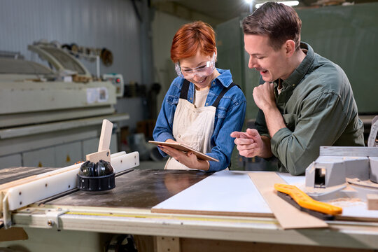 Young caucasian man and woman joiners using digital tablet while working in workshop, professional carpenters discussing working process, what to do, handmade and carpentry concept