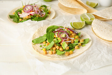 Parchment with tasty vegetarian tacos on light wooden background