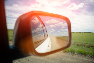 Reflection in the side mirror of dust from the wheels of a car moving on a country road close up.