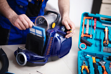 Handsome young serviceman is repairing modern vacuum cleaner in his office