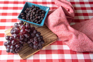 Fresh red grapes and raisins on a board with red checkered tablecloth background.