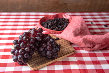 Fresh red grapes and raisins on a board with red checkered tablecloth background.