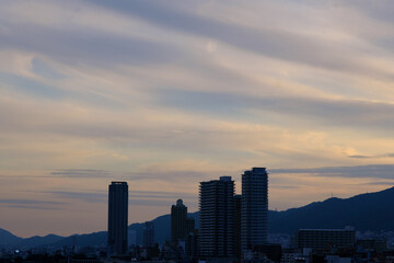 Fototapeta na wymiar 日の入り前の六甲山。西の空と雲がオレンジ色に染まるマジックアワー。高層ビルがシルエットで浮かぶ。１日の終わり。