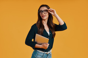 Confident young woman in smart casual clothing using digital tablet and adjusting eyewear