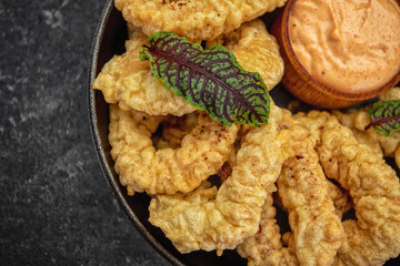 Golden rings of squid fries in a round frying pan with sauce, herbs and lemon on a dark background without decorations