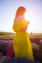 Beautiful and pretty young woman in yellow dress relaxes and enjoys walk in the lavender field at...