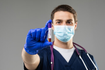 Young scientist investigates a blood test for coronavirus. Diagnostics 2019-ncov. positive blood test result for covid 19. Doctor with a blood sample on a gray background