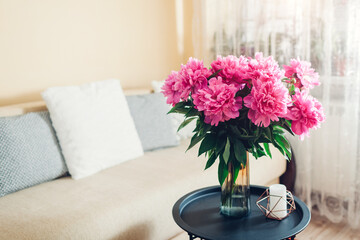 Interior and home decor. Fresh pink peonies flowers put in vase in living room. Bouquet of blooms on coffee table