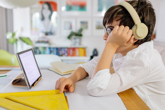 Concentrate pre-teen designing a project  on paper and using a tablet sitting at table